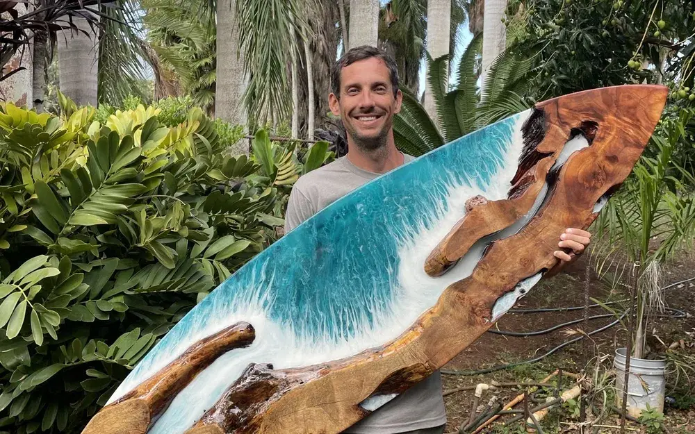 Big Island artist Seth Greene holding a resin and wood surfboard he made, creator of the bar top at Jackie Rey's Kona.
